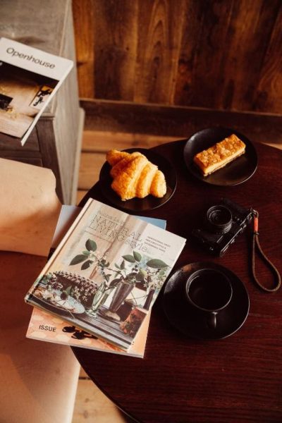 Mesa de desayuno con croissant, café, cámara y revistas en el Glasson Lakehouse
