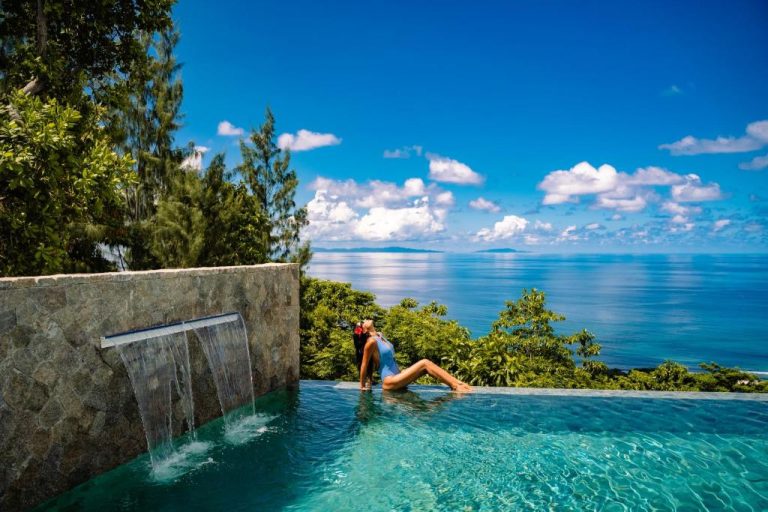 Piscina infinita con cascada y vistas al océano en AQUA Boutique Hotel, rodeada de vegetación tropical