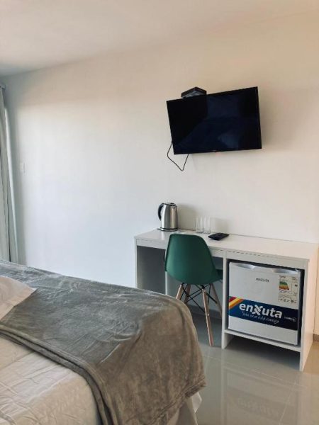Habitación del PLC Hotel Centenario con TV de pared, escritorio blanco, silla verde y minibar Enxuta