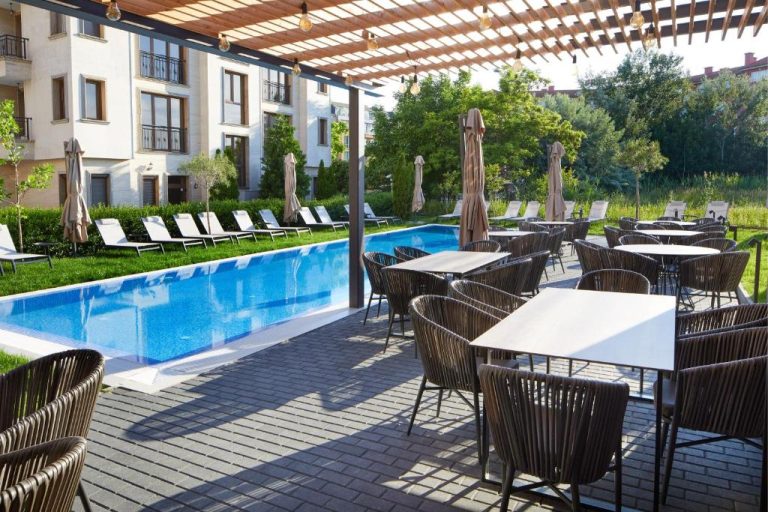 Terraza con mesas y sillas junto a la piscina exterior del Amara Sugar Hotel rodeada de jardines