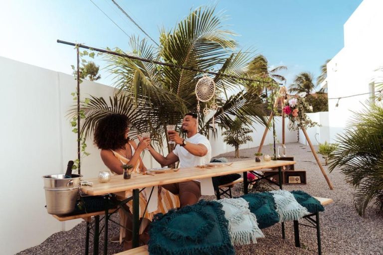 Pareja brindando en cena romántica al aire libre con decoración boho en The Palm Leaf Apartments