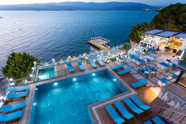 Piscina exterior iluminada con tumbonas azules y restaurante frente al mar en Güllük Yalı Boutique Otel
