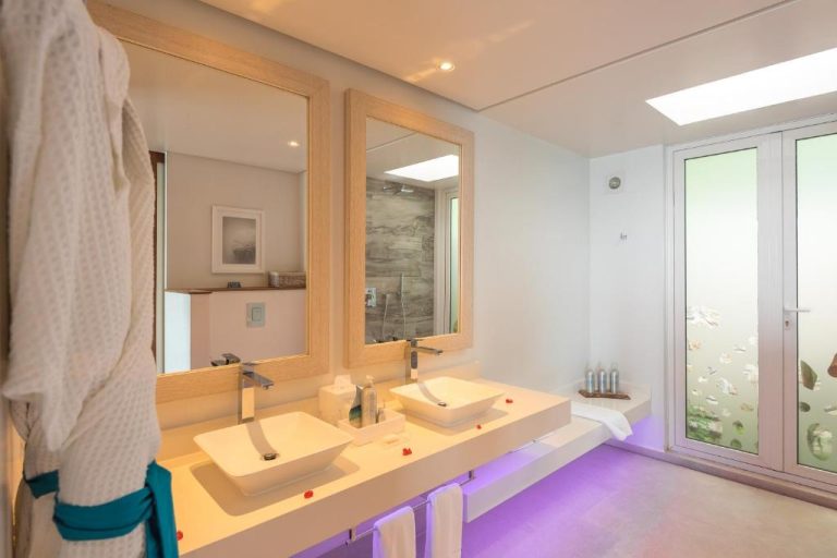 Baño de lujo con doble lavabo y luz ambiental morada en el hotel CaranaBeach