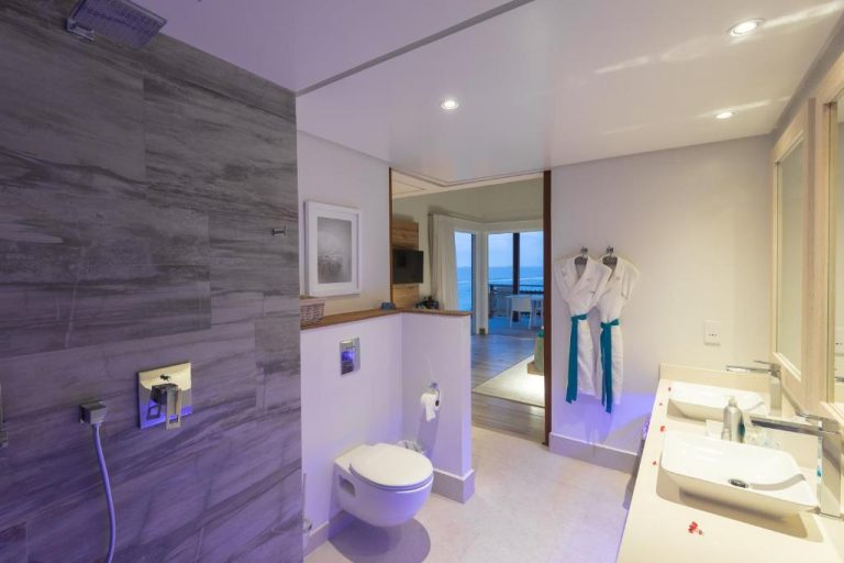 Baño moderno con ducha de lluvia y batas de baño en Hotel CaranaBeach con vista al mar