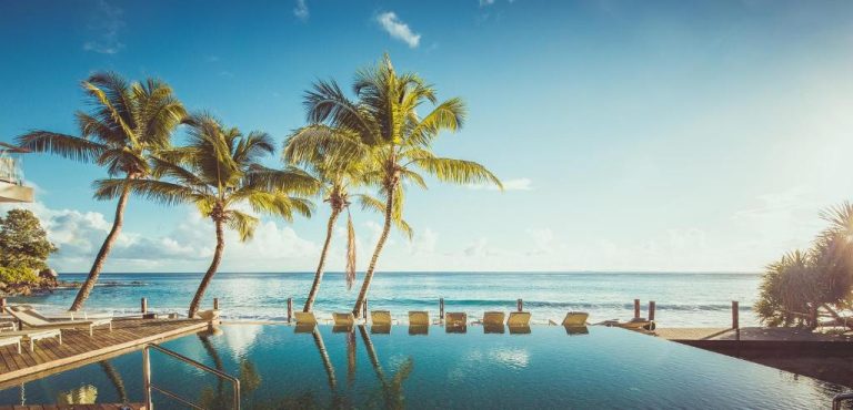 Piscina infinita con palmeras tropicales y vistas al océano turquesa en CaranaBeach Hotel