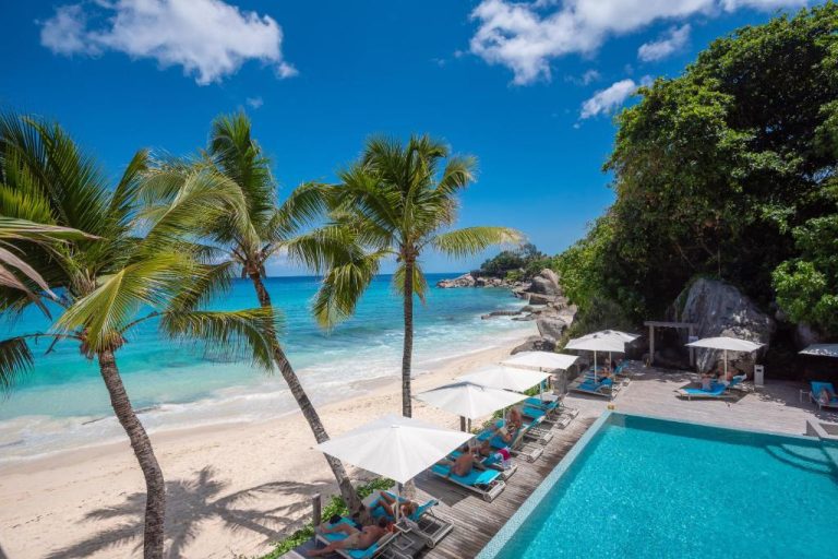 Piscina infinita y playa de arena blanca con palmeras tropicales en el hotel CaranaBeach Seychelles