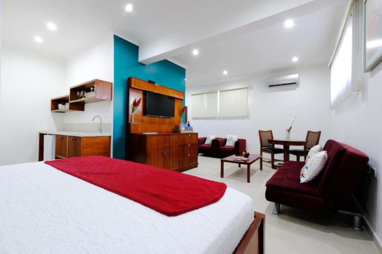 Suite del Victoria City Hotel con cama doble, sofás burdeos, cocina americana y televisión empotrada
