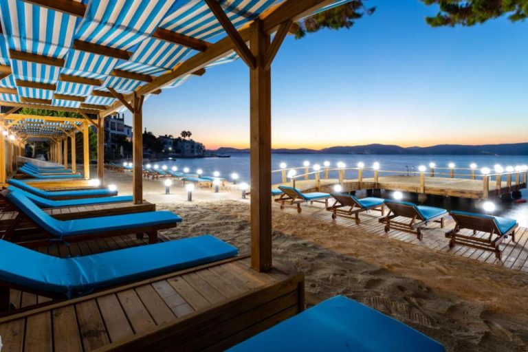 Tumbonas azules en la playa privada con muelle iluminado al atardecer del Güllük Yalı Boutique Otel