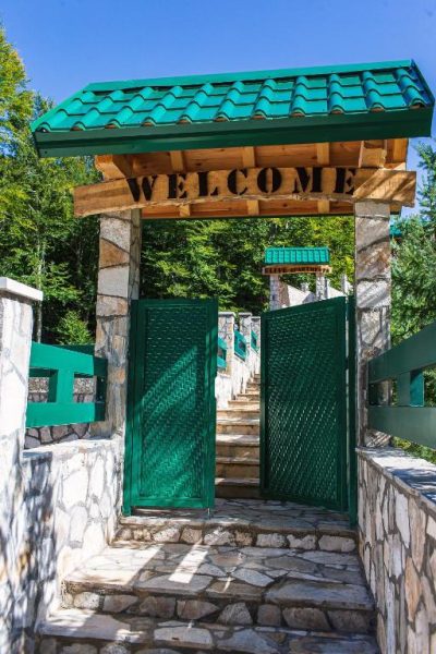 Entrada principal con puerta verde y cartel de bienvenida del Garni Hotel Elite Resort rodeado de naturaleza
