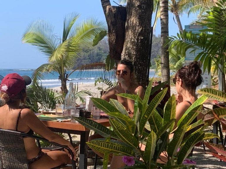 Turistas disfrutando del restaurante terraza frente al mar en Beach Front Bahia con palmeras y playa