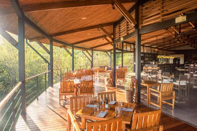 Terraza restaurante con mesas de madera y vistas al bosque tropical en Rio Perdido Hotel & Thermal River