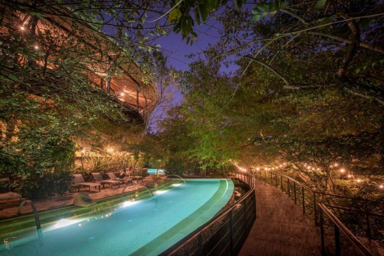 Piscina infinita iluminada de noche rodeada de vegetación tropical en Rio Perdido Hotel & Thermal River