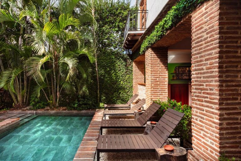 Piscina exterior con tumbonas de madera y jardín tropical en Hotel Villa Colonial