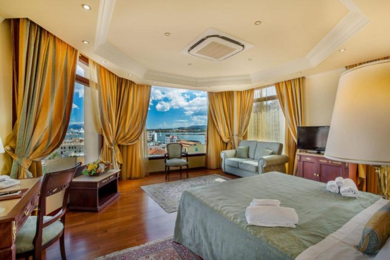 Suite de lujo con vistas al mar y puerto en Hotel Panorama, decorada con cortinas doradas y cama king size