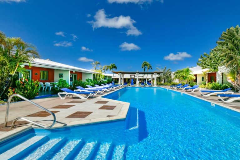 Piscina exterior con tumbonas azules y palmeras del Aruba Blue Village Hotel and Apartments