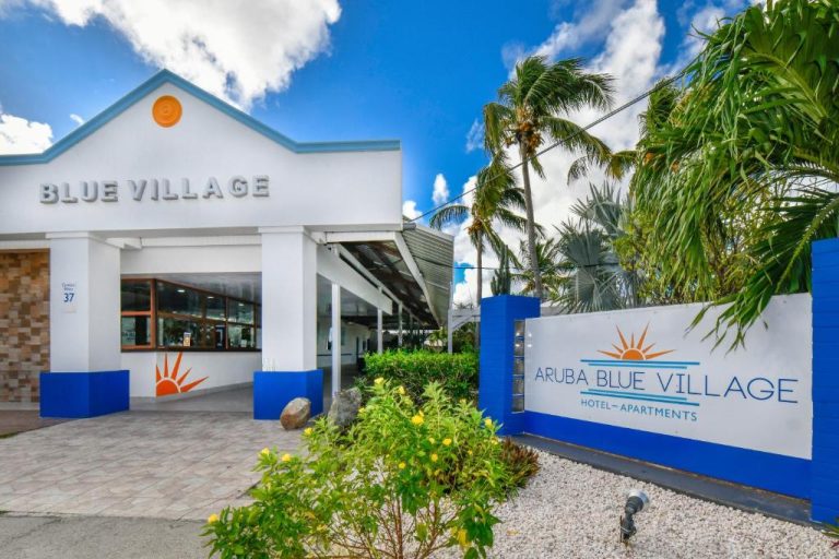 Fachada principal y entrada del Aruba Blue Village Hotel and Apartments con palmeras y jardín