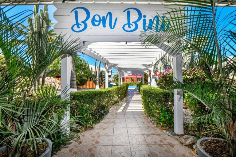 Entrada principal con pérgola blanca y jardín tropical del Aruba Blue Village Hotel and Apartments