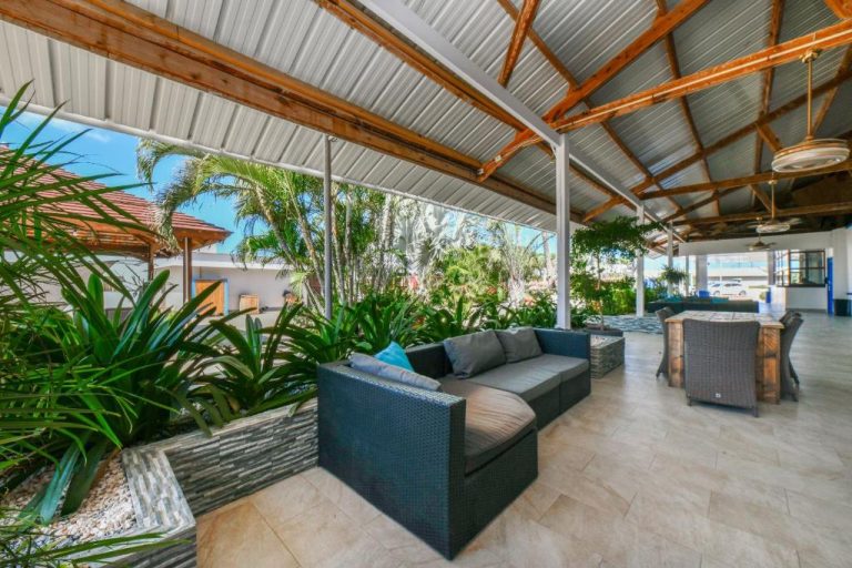 Terraza lounge exterior con sofás y vegetación tropical en Aruba Blue Village Hotel and Apartments
