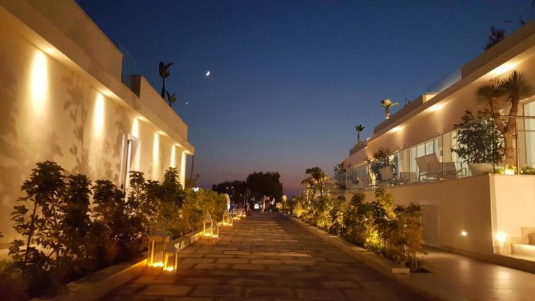 Paseo de acceso iluminado con faroles y jardines del Modica Beach Resort al atardecer