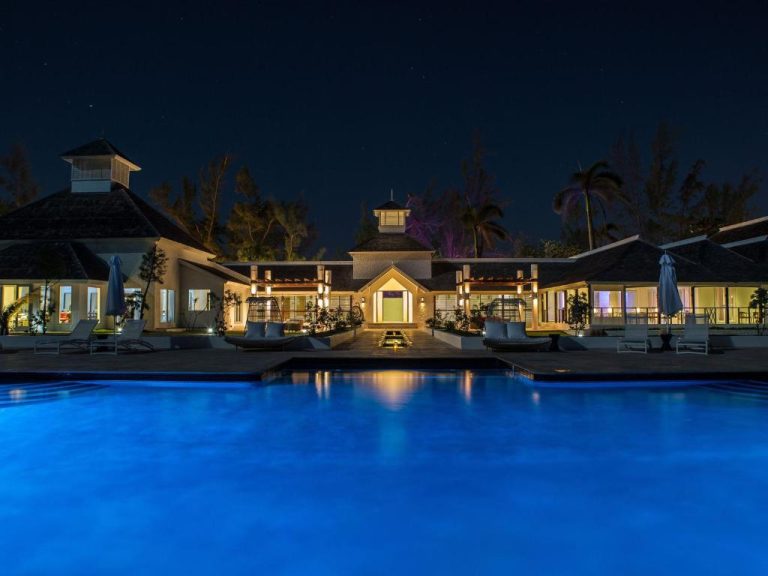 Piscina exterior iluminada de noche en The Trident Hotel con vistas a la elegante fachada del resort