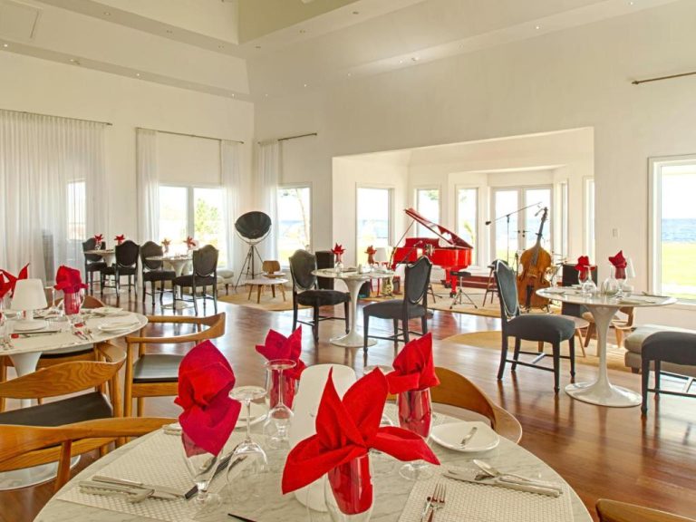Elegante restaurante del The Trident Hotel con piano de cola rojo, mesas con servilletas rojas y vistas al mar