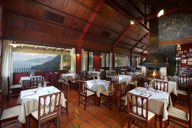 Restaurante del Hotel Quinta do Furao con mesas elegantes, chimenea y vistas panorámicas a la montaña y al mar