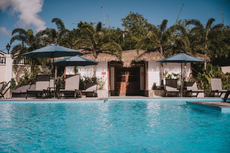 Piscina exterior con tumbonas y sombrillas del Hotel Bambou rodeada de palmeras tropicales