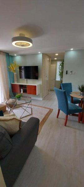 Sala de estar y comedor moderno en Almond Grove at Sand Castle con TV, sillas azules y decoración tropical