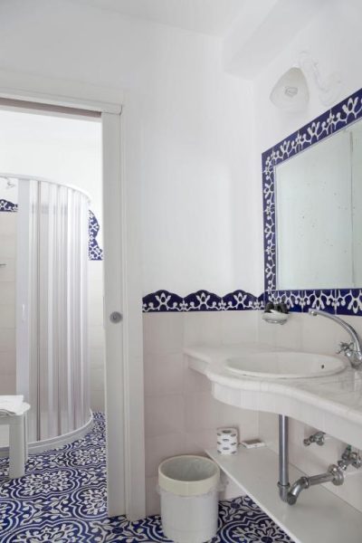Baño con azulejos azules y blancos, lavabo clásico y ducha en Hotel La Terrazza