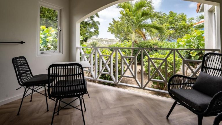 Terraza con sillas de ratán negras y vistas al jardín tropical en Blue Bay Lodges Curazao