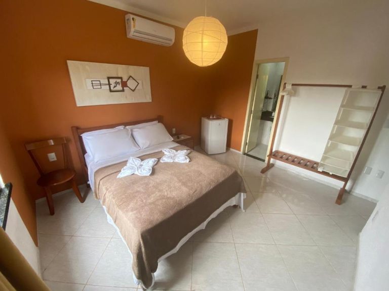 Habitación doble con pared naranja, cama matrimonial y baño privado en Refúgio Pousada Fortaleza