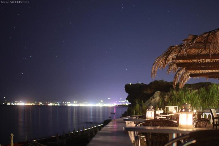 Terraza nocturna del Crystal Beach Hotel con vistas al mar iluminado y cielo estrellado