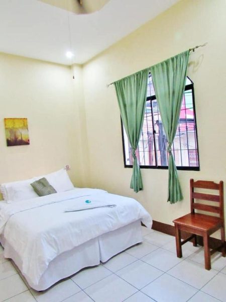 Habitación doble con cama matrimonial y ventana con cortinas verdes en Hotel Palmeras de Elim