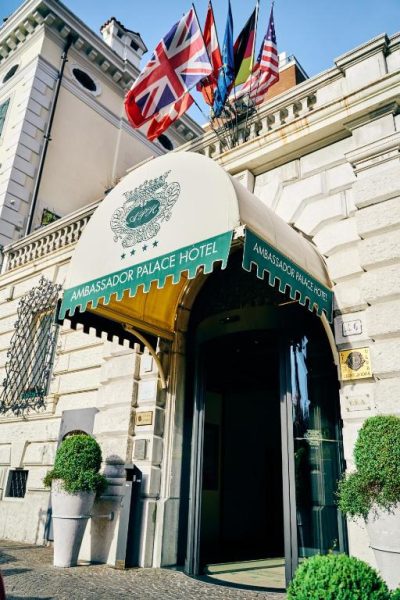 Entrada principal del Ambassador Palace Hotel con toldo verde y banderas internacionales en la fachada