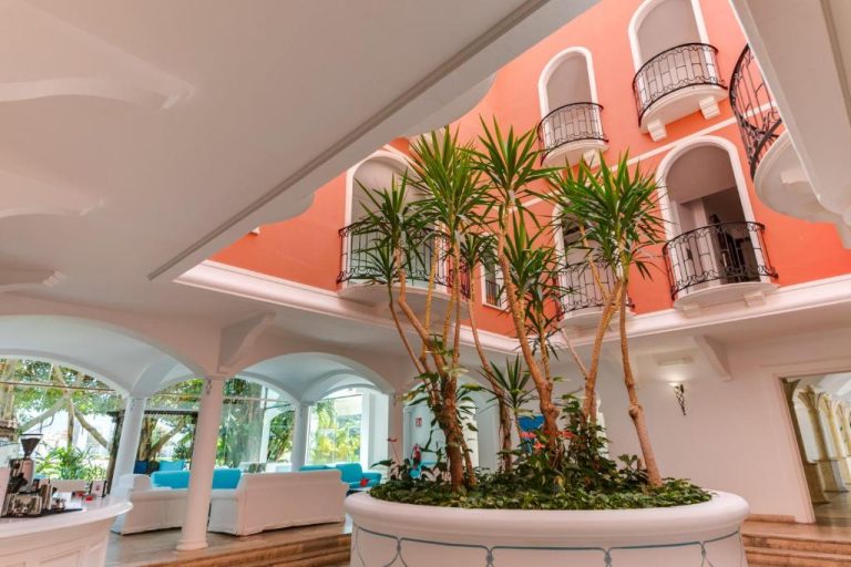 Atrio interior con palmeras y balcones del Phi Hotel Sighientu, decorado en tonos coral y blanco