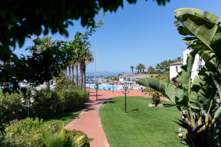 Jardines y piscina exterior del Phi Hotel Sighientu con palmeras y vistas al mar en Cerdeña