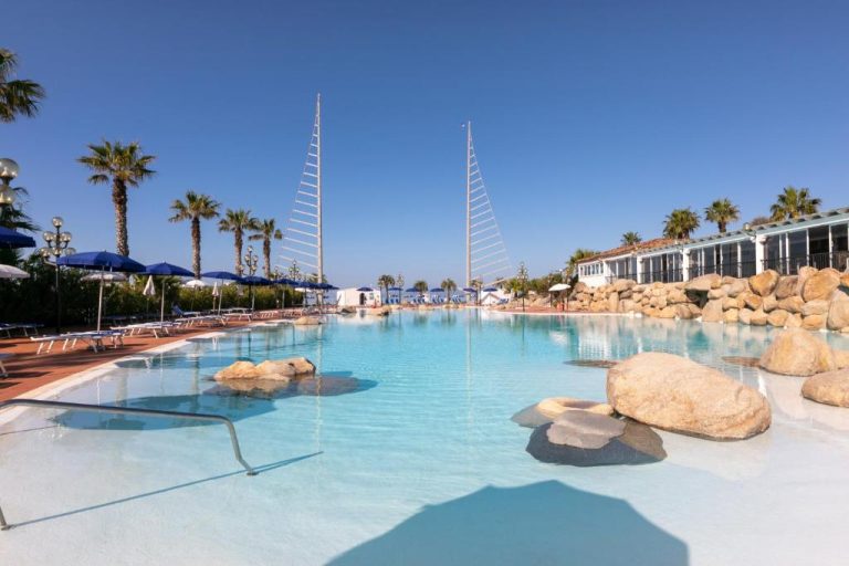 Piscina exterior con rocas naturales y palmeras del Phi Hotel Sighientu en Cerdeña