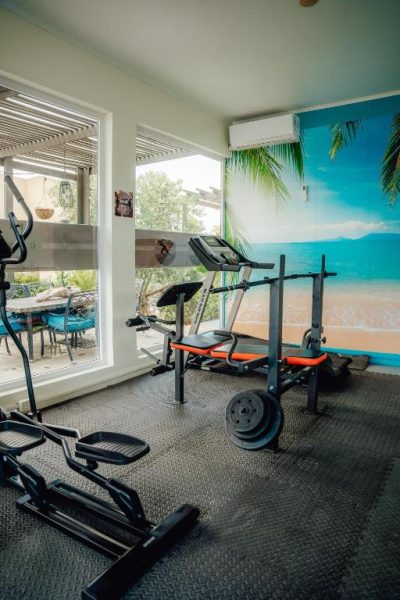 Gimnasio equipado con máquinas de ejercicio y mural de playa tropical en Hotel RH Boutique Aruba