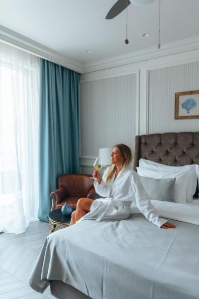 Mujer en bata de baño disfrutando copa de vino blanco en habitación de lujo del Boutique Hotel Casa del Mare Vizura