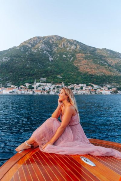 Mujer en barco de madera frente a la bahía de Kotor con el Boutique Hotel Casa del Mare Vizura al fondo