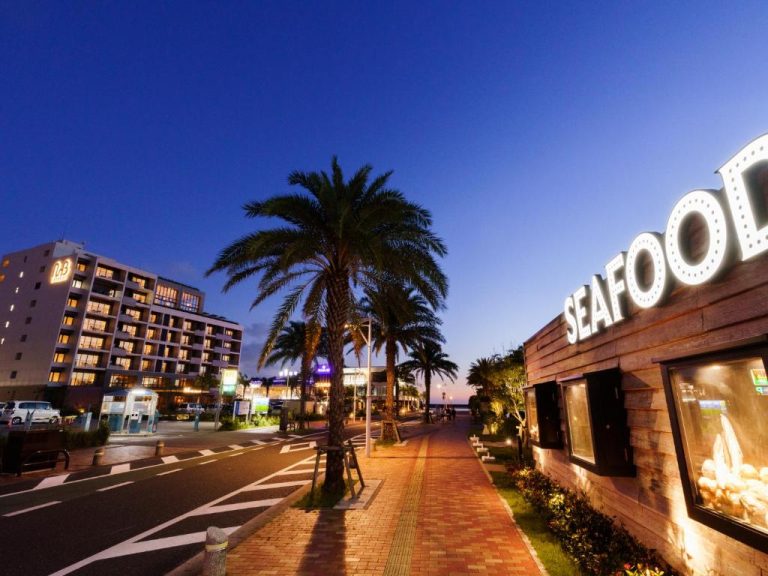 Paseo marítimo nocturno con palmeras y restaurante de mariscos junto al MB Gallery Chatan by The Terrace Hotels