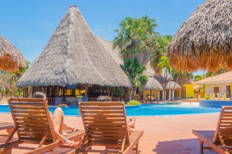 Piscina exterior con palapas de palma y tumbonas de madera en el Nandel Beach Resort