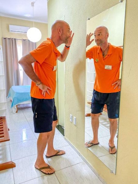 Miembro del personal de Refúgio Pousada Fortaleza con polo naranja frente al espejo en zona interior