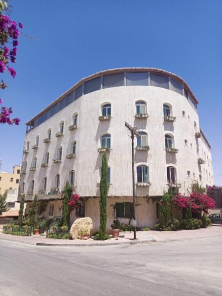 Fachada exterior del Mariam Hotel, edificio redondeado de piedra blanca con balcones y jardines floridos
