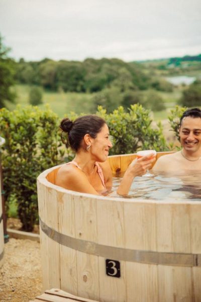Pareja disfrutando de un baño en barril de madera exterior con vistas al lago en Glasson Lakehouse