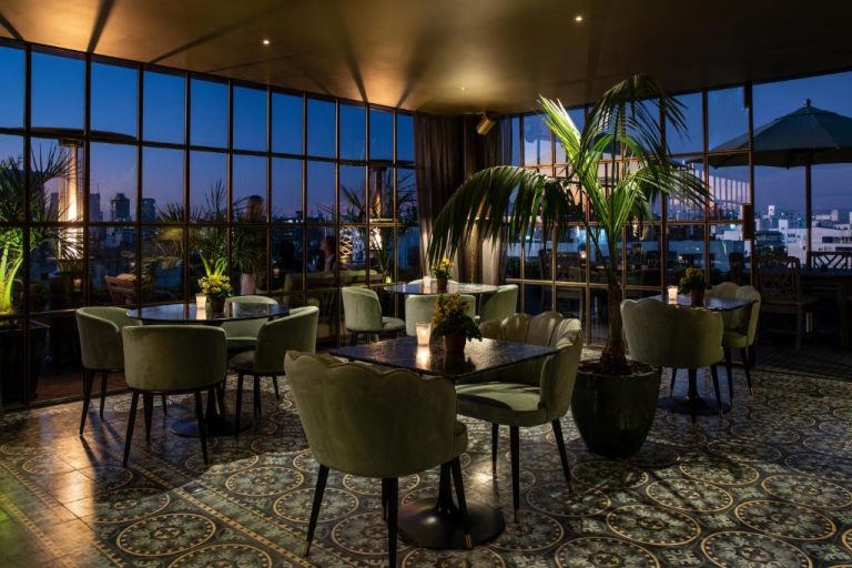 Elegante rooftop bar con sillones de terciopelo verde y vistas panorámicas nocturnas en Hotel Montevideo Leading Hotels