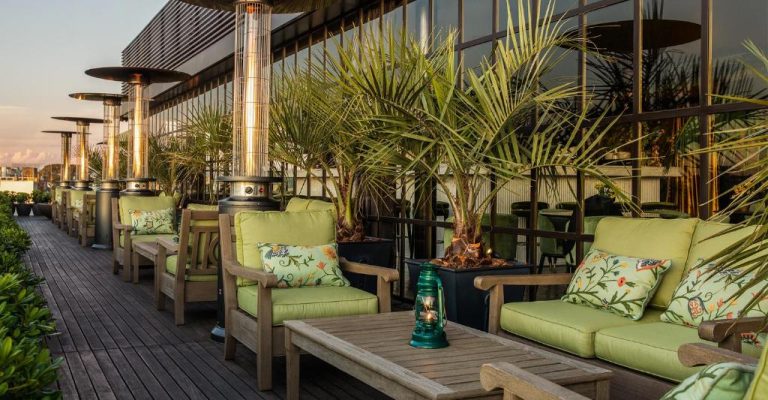 Terraza lounge exterior del Hotel Montevideo con sillones verdes, palmeras y calefactores al atardecer