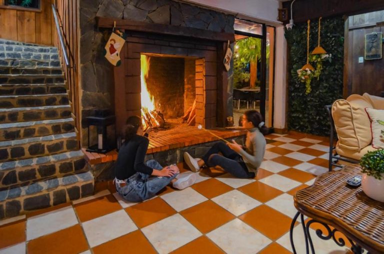 Dos huéspedes sentadas frente a la chimenea encendida en el salón del Hotel Rancho Constanza & Cabañas de la Montaña