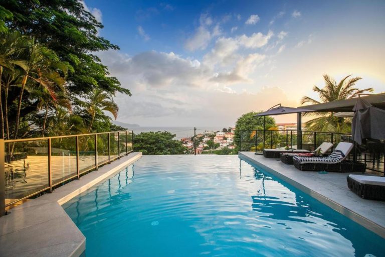 Piscina infinita con vistas al mar y ciudad en el Karibea Squash Hôtel, rodeada de palmeras