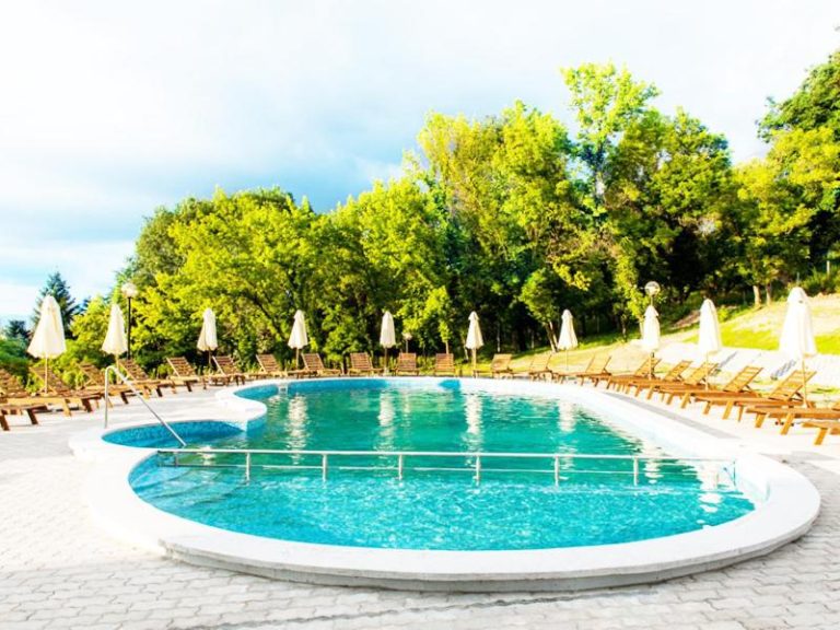 Piscina exterior con tumbonas y sombrillas del Park Hotel Kyustendil rodeada de jardín
